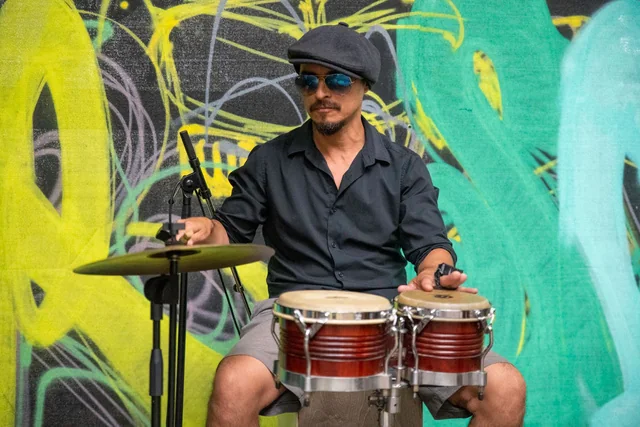 Greco Acuña playing percussion in front of a colorful mural
