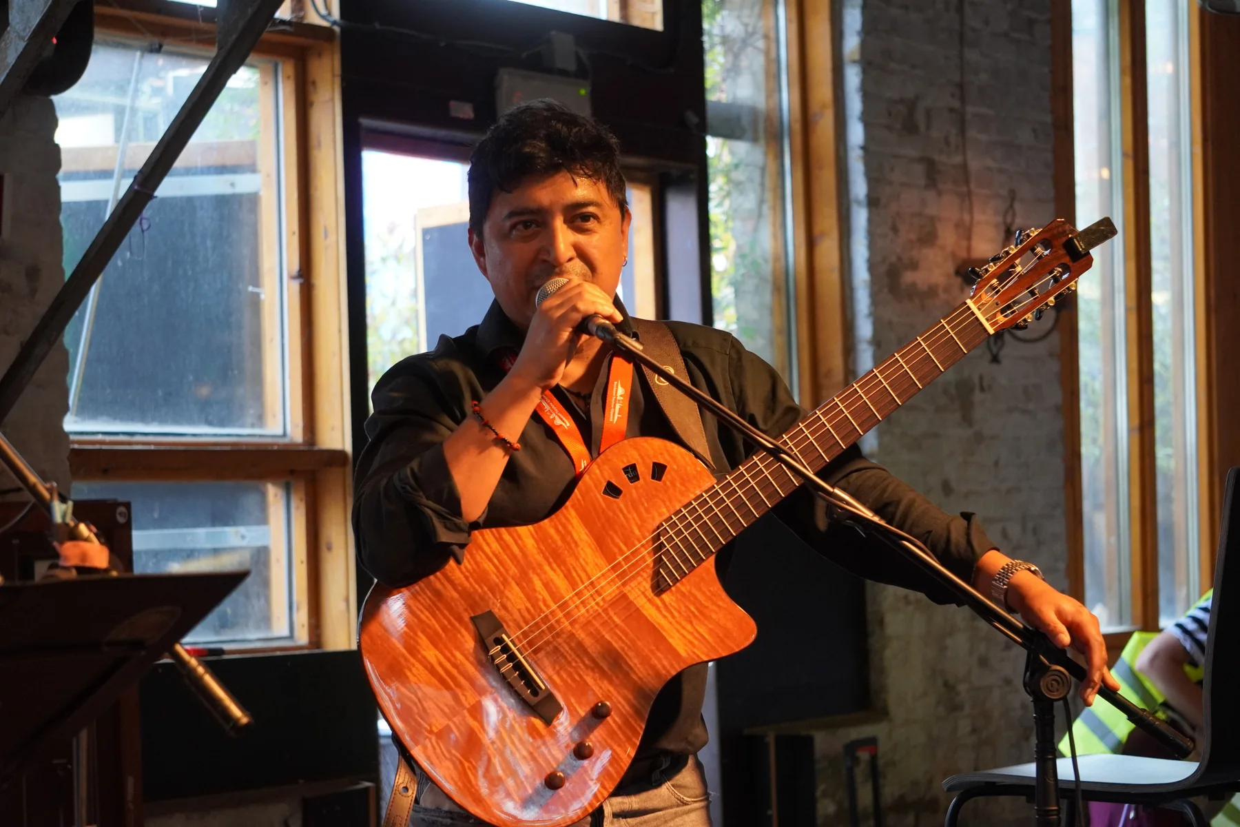José Carlos Mayorga speaking into a microphone with his guitar